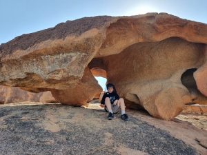 Logan is sitting under an spectacularly eroded rock. The rock has aboriginal artwork on the roof.